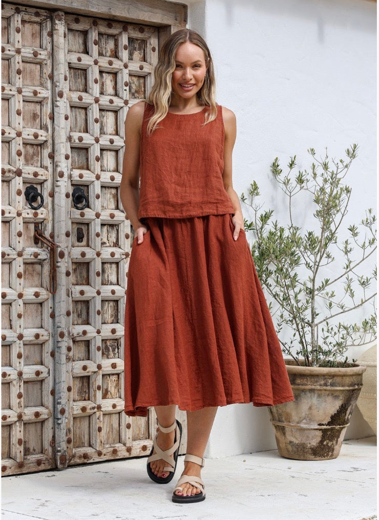 Woman in a rust-colored sleeveless top and skirt standing in front of a wooden door.